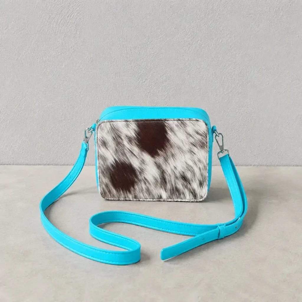 Leather cowhide box style crossbody bag with turquoise strap, brown and white cowhide texture, structured purse design and adjustable shoulder strap