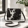 Dark brown and white cowhide mobile phone pouch square style with zipper pocket, adjustable shoulder strap and leather tassel detail