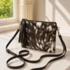 Dark brown and white cowhide mobile phone pouch square style with zipper pocket, adjustable shoulder strap and leather tassel detail
