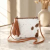 Cowhide mobile phone pouch square style with brown and white cowhide pattern, tan leather strap, zipper pocket and adjustable shoulder strap