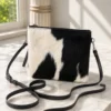 Cowhide mobile phone pouch square style with brown and white cowhide pattern, tan leather strap, zipper pocket and adjustable shoulder strap